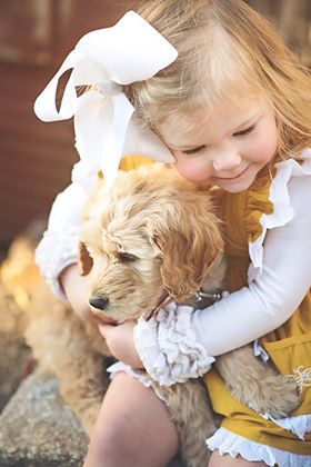 Cute little girl wearing a yellow and white dress hugging her golden wavy coat puppy.